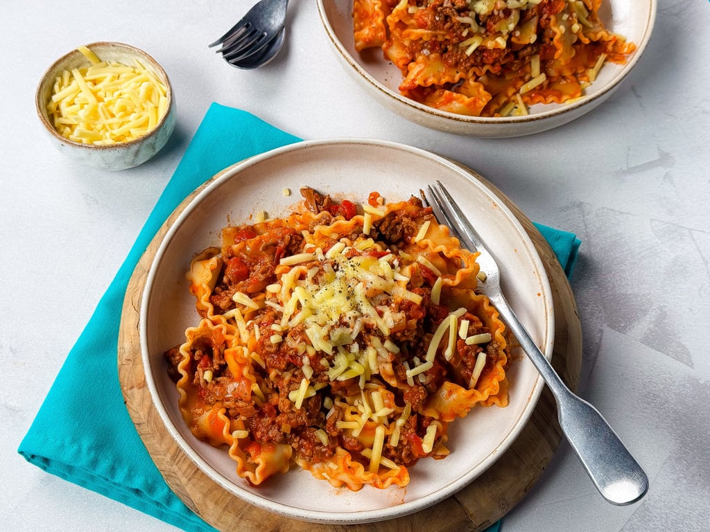 Two plates of pasta with meat sauce and grated cheese, fork on one plate, bowl of cheese