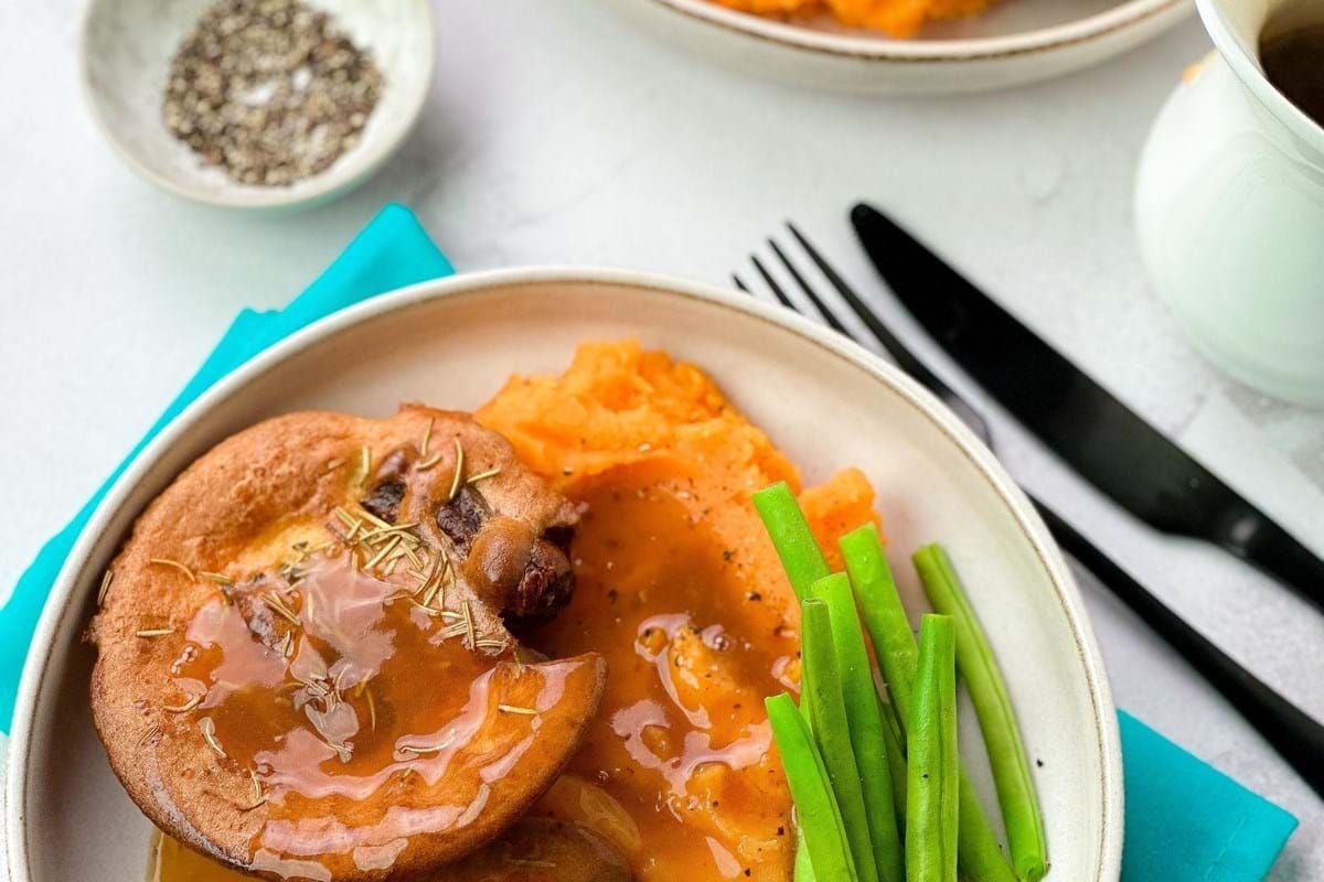 Yorkshire puddings with gravy, mashed sweet potatoes, and green beans on plates