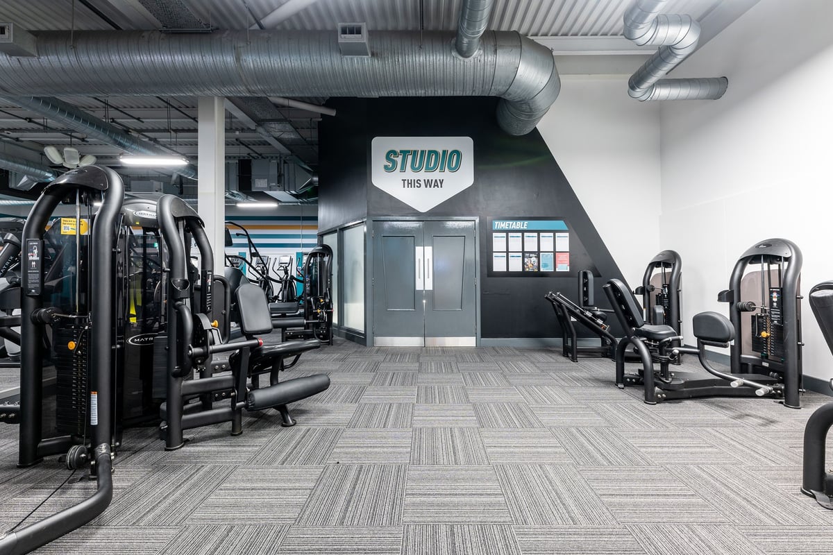 PureGym Cambridge Leisure Park: Rows of resistance machines, weight benches, and rubberized flooring in studio-style gym space.