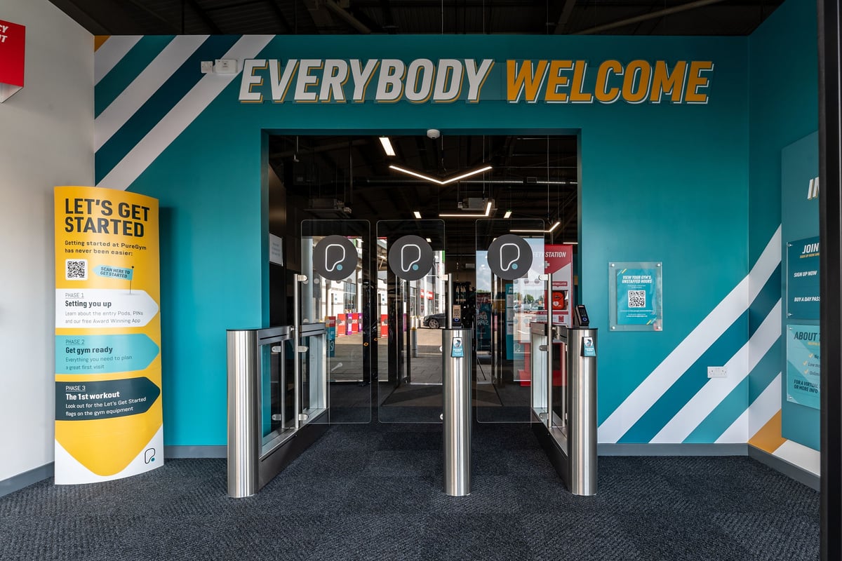 PureGym Durham City Retail Park: Entrance turnstiles with "EVERYBODY WELCOME" signage, notice boards, and teal blue branding.