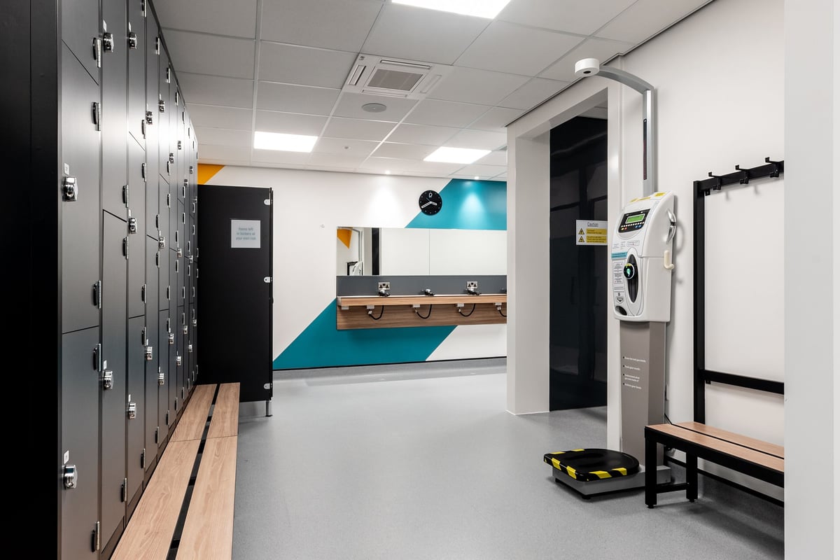 PureGym Kettering: Lockers, benches, weights, turf area, mirrors along walls - typical gym changing room setup.