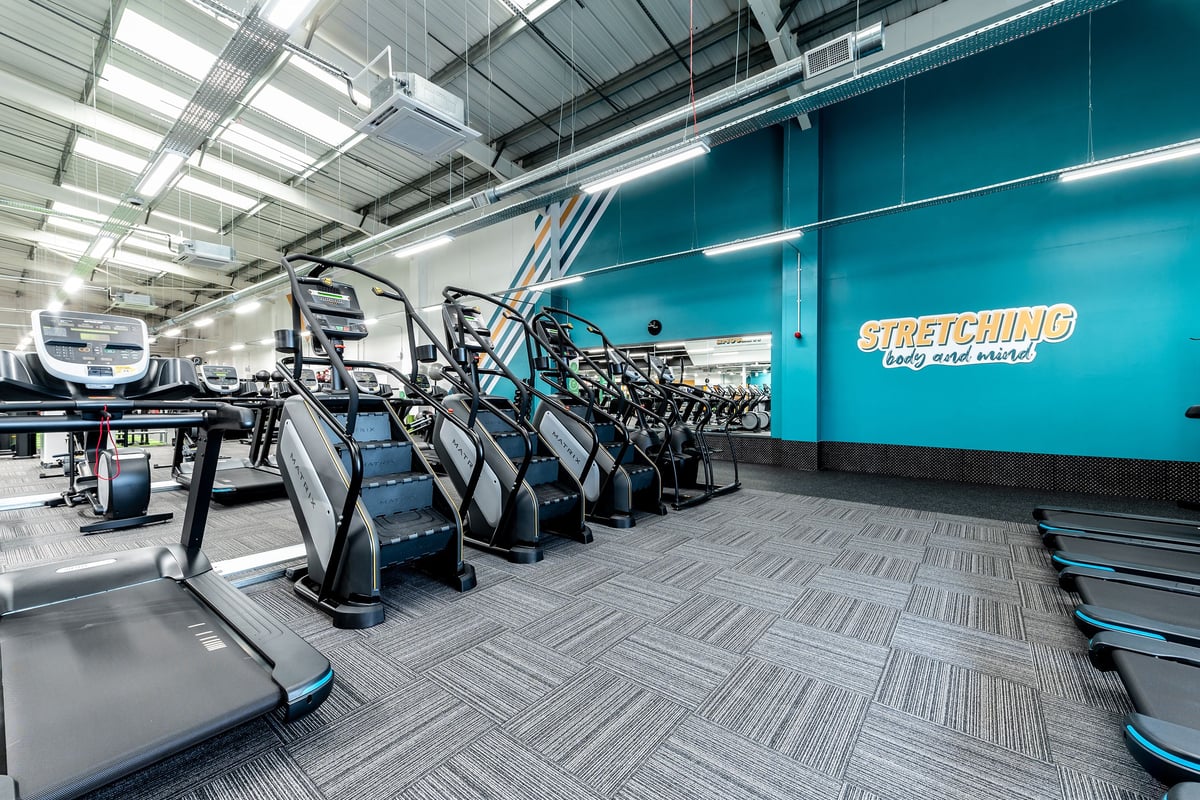 PureGym Ashford Warren Retail Park: Rows of treadmills and exercise bikes lining a blue-tinted gym interior.