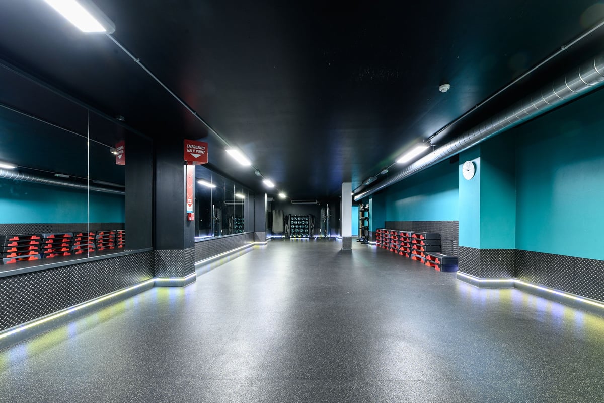 PureGym London Greenwich: Rows of red benches, futuristic lighting, and a long hallway-like space.