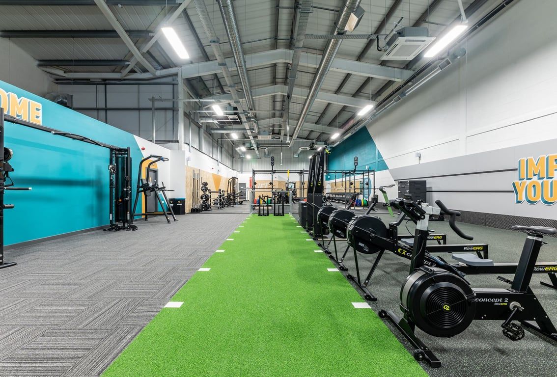 PureGym Byfleet: Rows of cardio machines, green turf area, free weights, and studio backdrop.