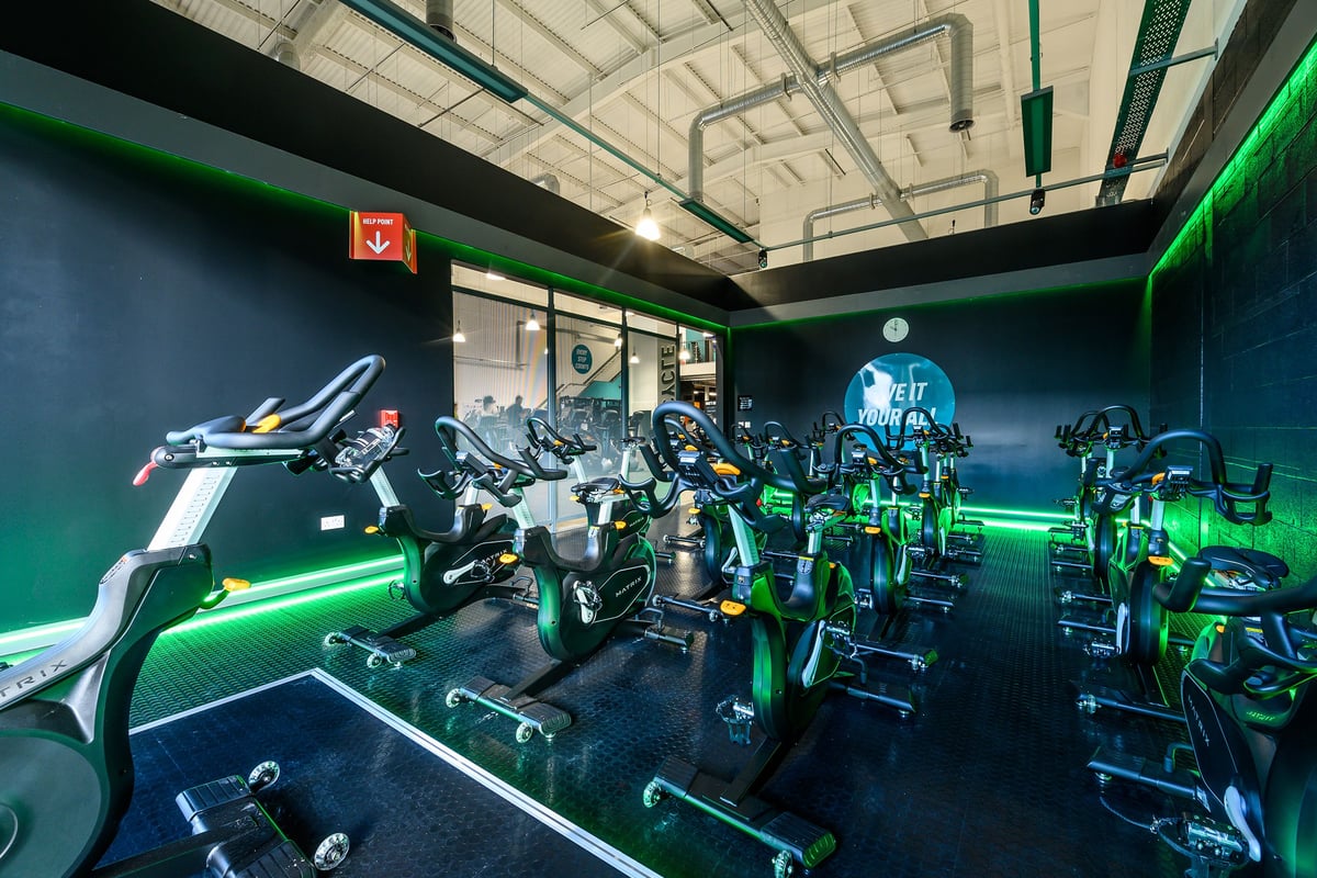 PureGym Romford: Futuristic gym with weightlifting machines, green accent lighting, and mirrored walls.