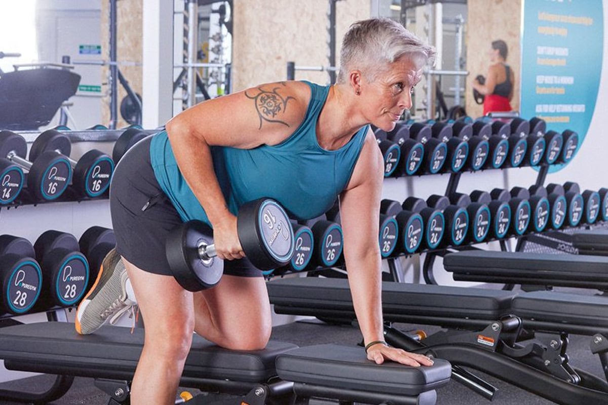 Woman lifting dumbbell on bench in gym with rows of weights behind her