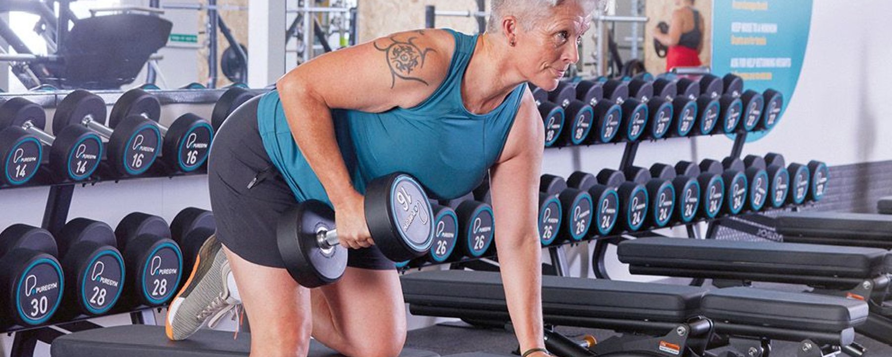 Woman lifting dumbbell on bench in gym with rows of weights behind her