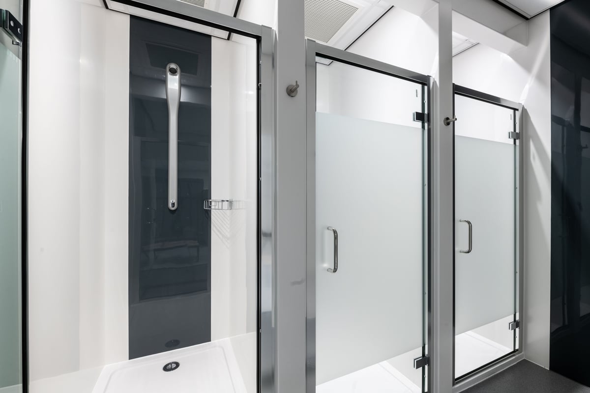 PureGym London Kingston: Glass paneled shower stalls with metal handles and narrow entrance doors.