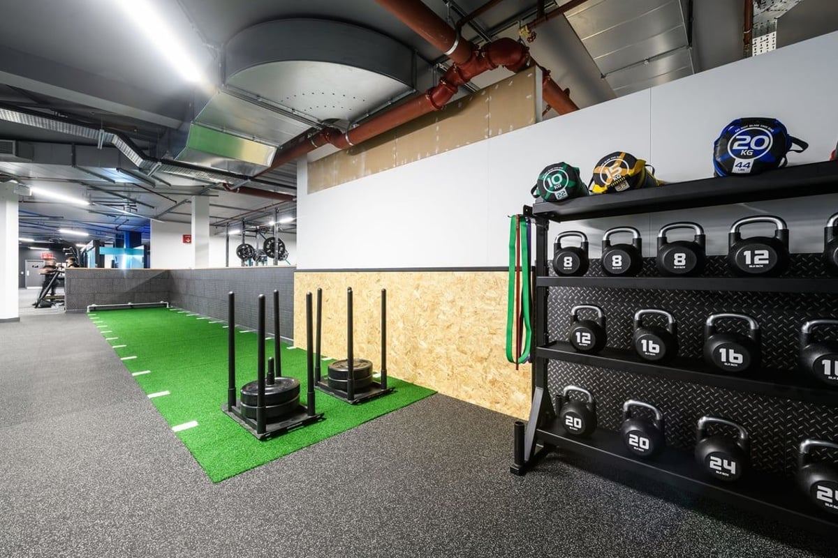 PureGym Basildon: Weight racks, medicine balls, plyo boxes, and rubberized green turf in a basement gym.