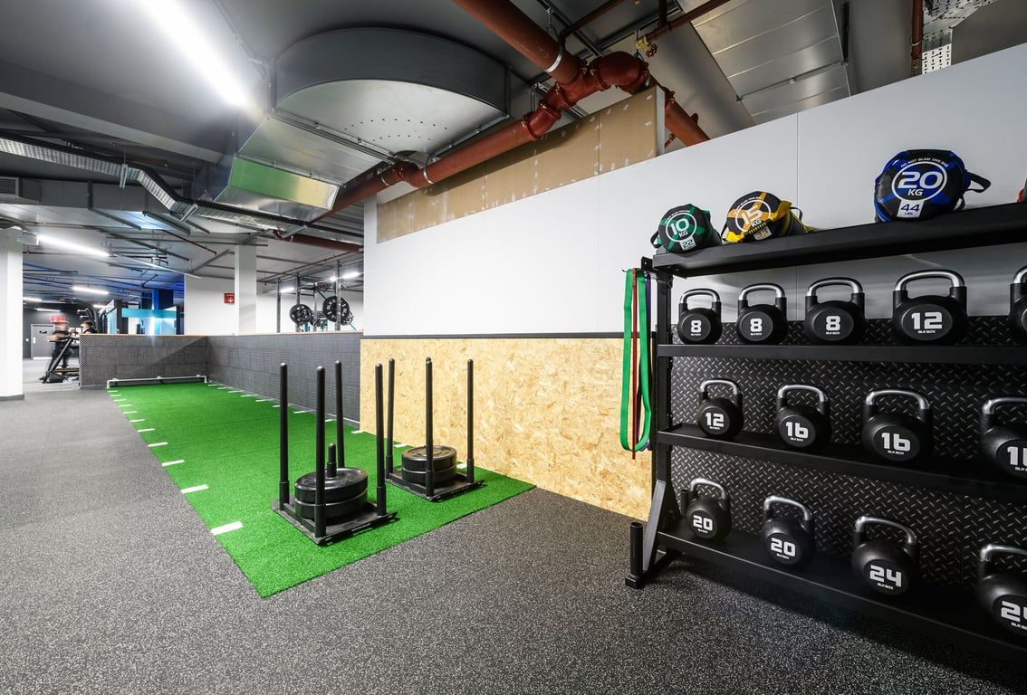 PureGym Basildon: Weight racks, medicine balls, plyo boxes, and rubberized green turf in a basement gym.