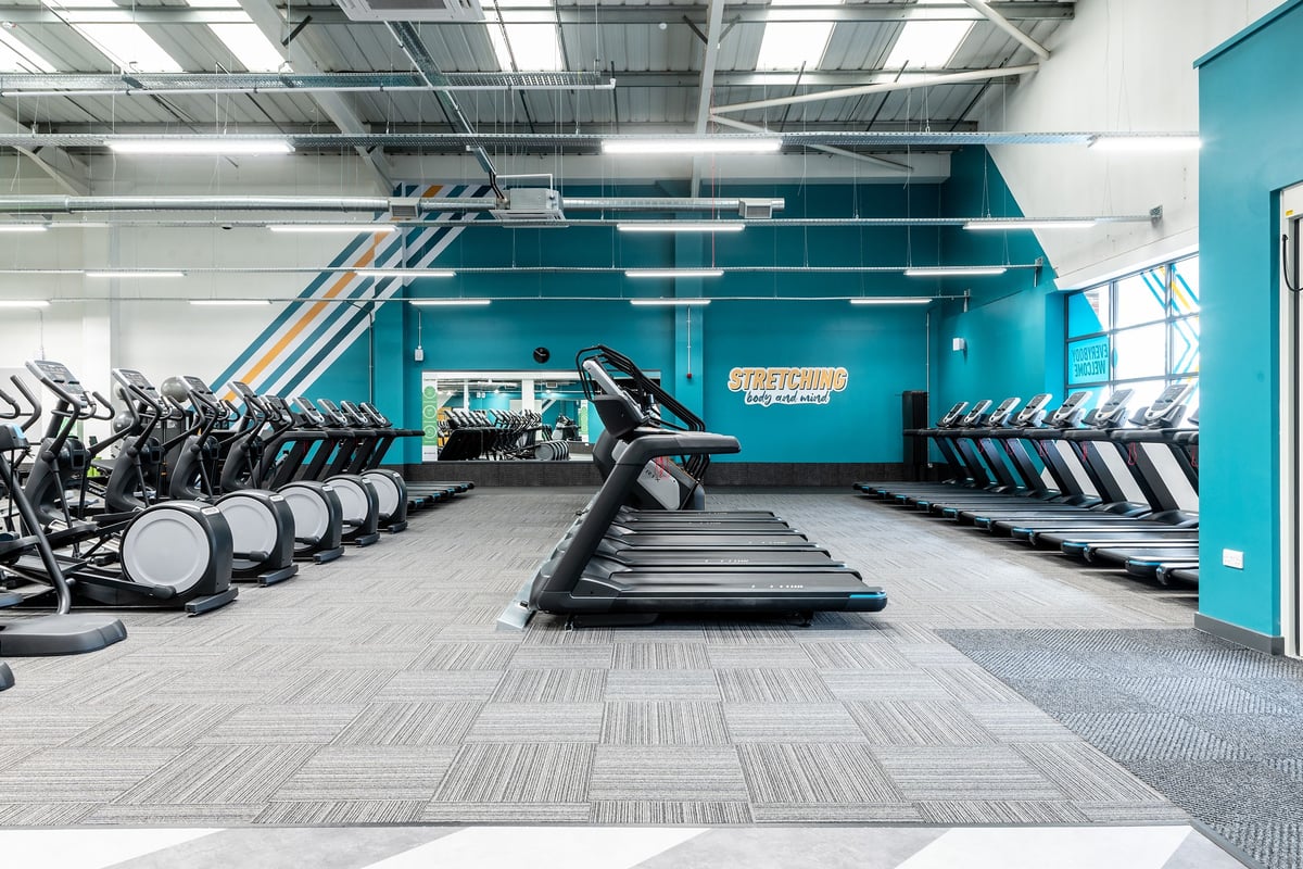 PureGym Ashford Warren Retail Park: Rows of treadmills, exercise bikes, and weight racks in a brightly lit gym interior.