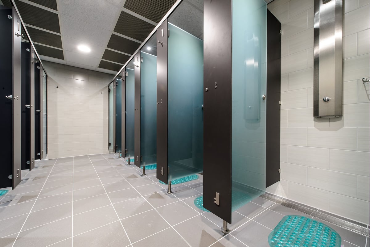 PureGym London Wembley: Rows of shower cubicles in blue and grey tones, with tiled flooring.