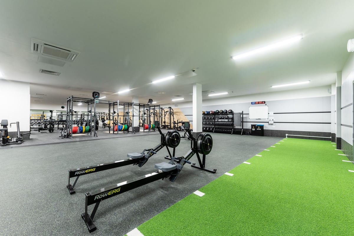 PureGym Tyldesley: Functional training area with squat racks, barbells, weight plates, turf zone, and rubberized flooring.
