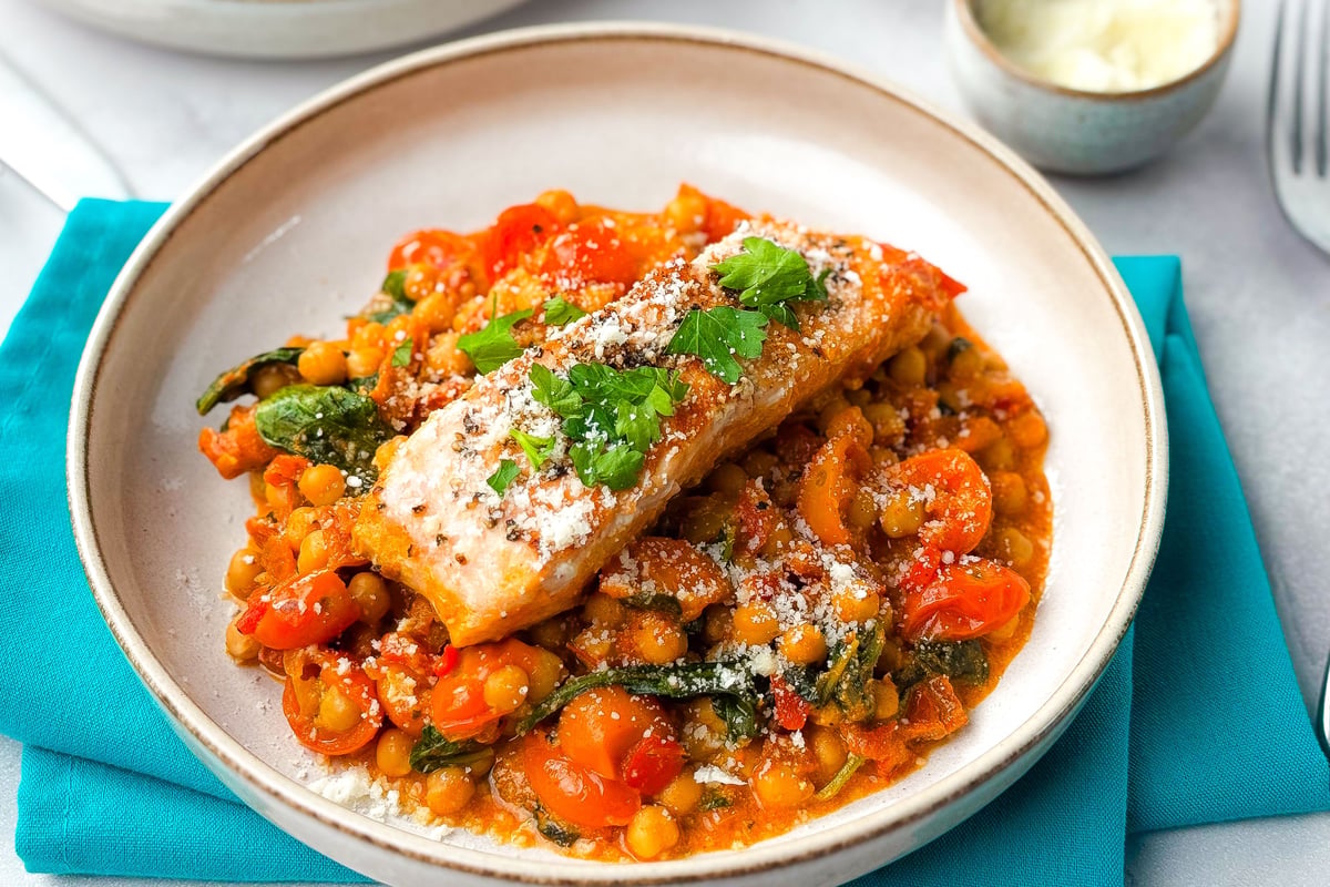 Piece of cooked salmon topped with fresh herbs on a bed of chickpeas and tomatoes
