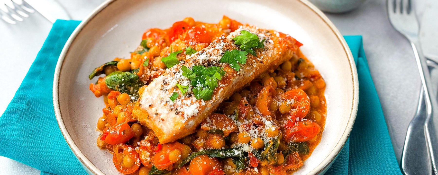 Piece of cooked salmon topped with fresh herbs on a bed of chickpeas and tomatoes