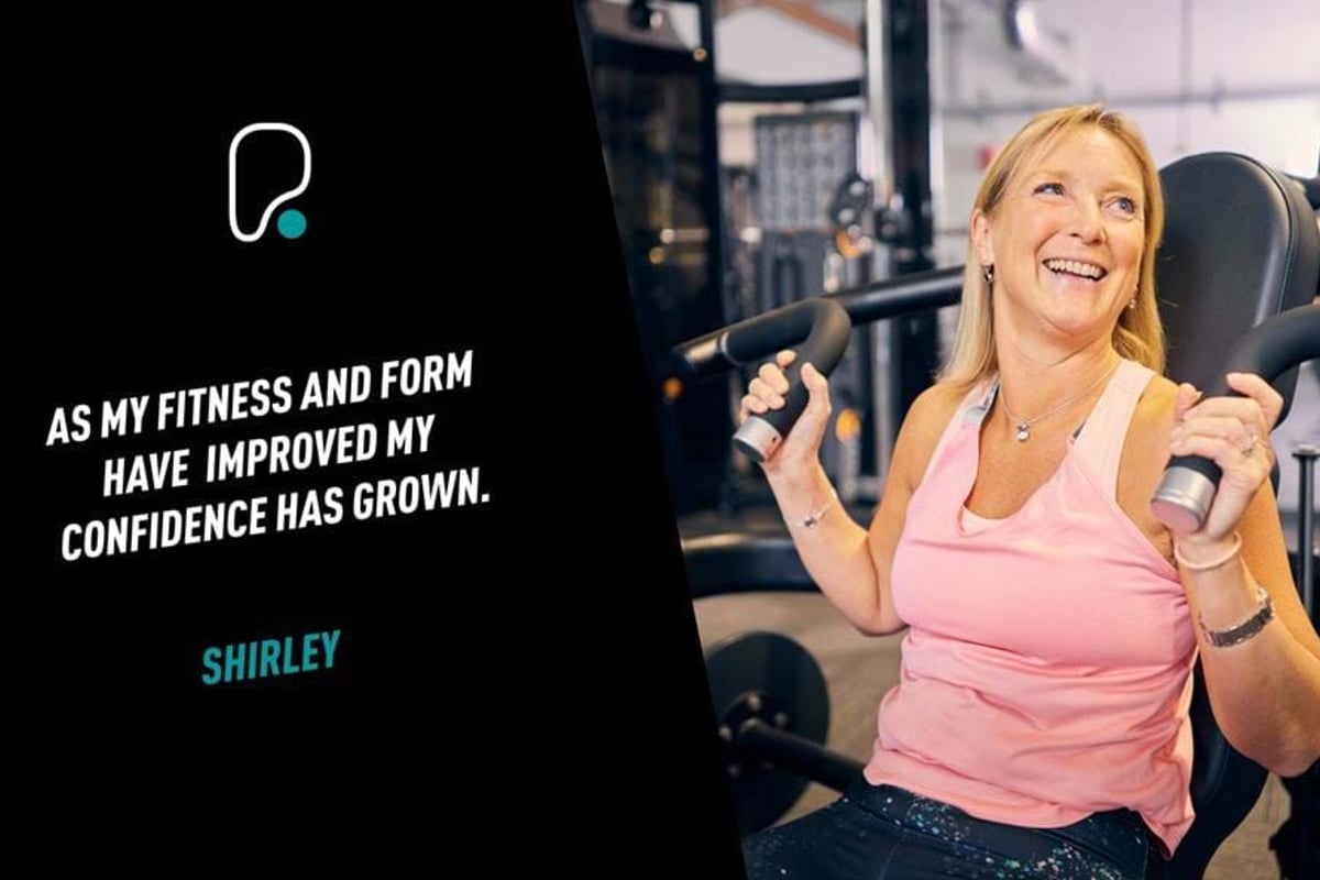 Woman in pink top using gym machine and smiling in fitness centre.