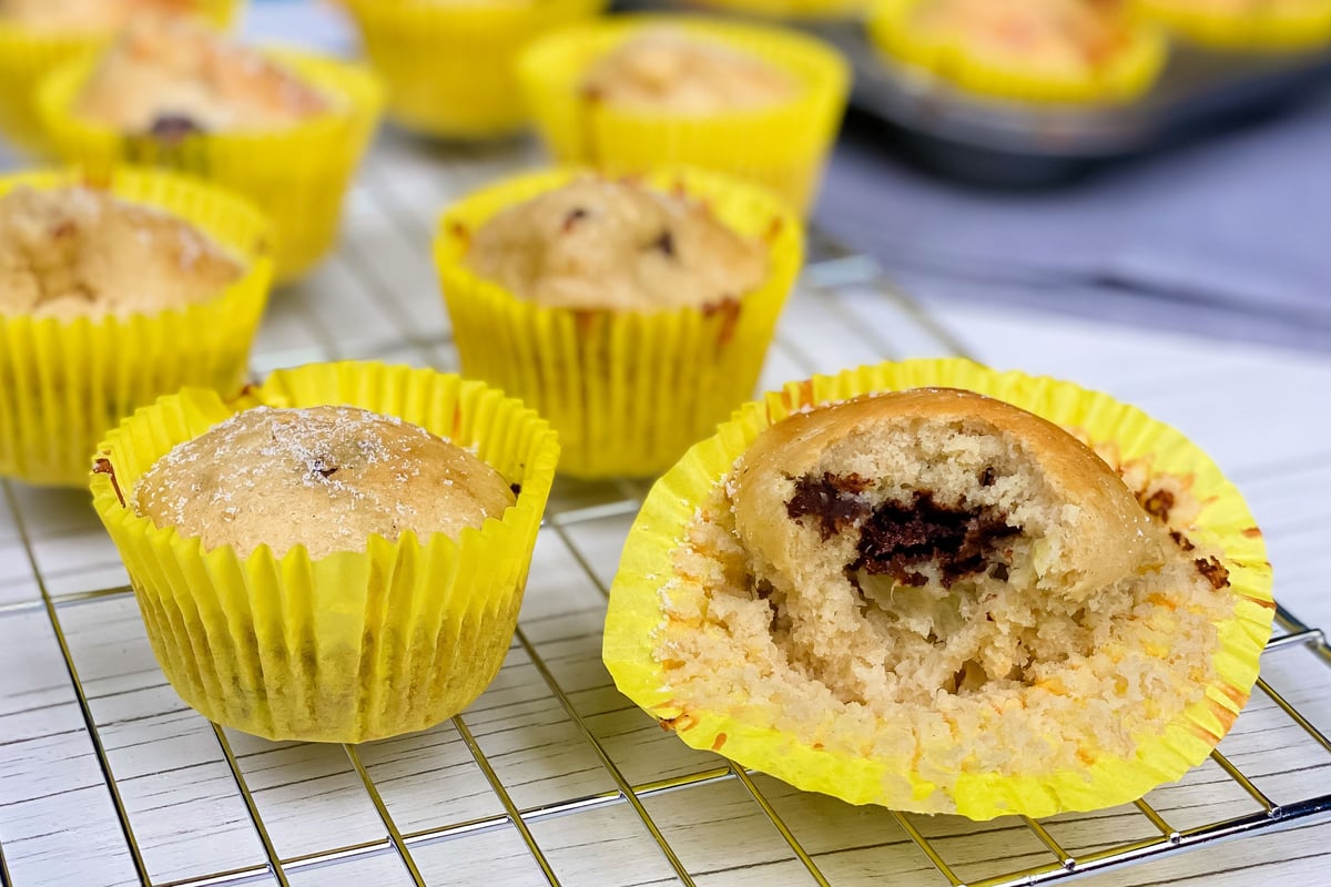 Mini muffins with dark chocolate filling in yellow cases on a cooling rack