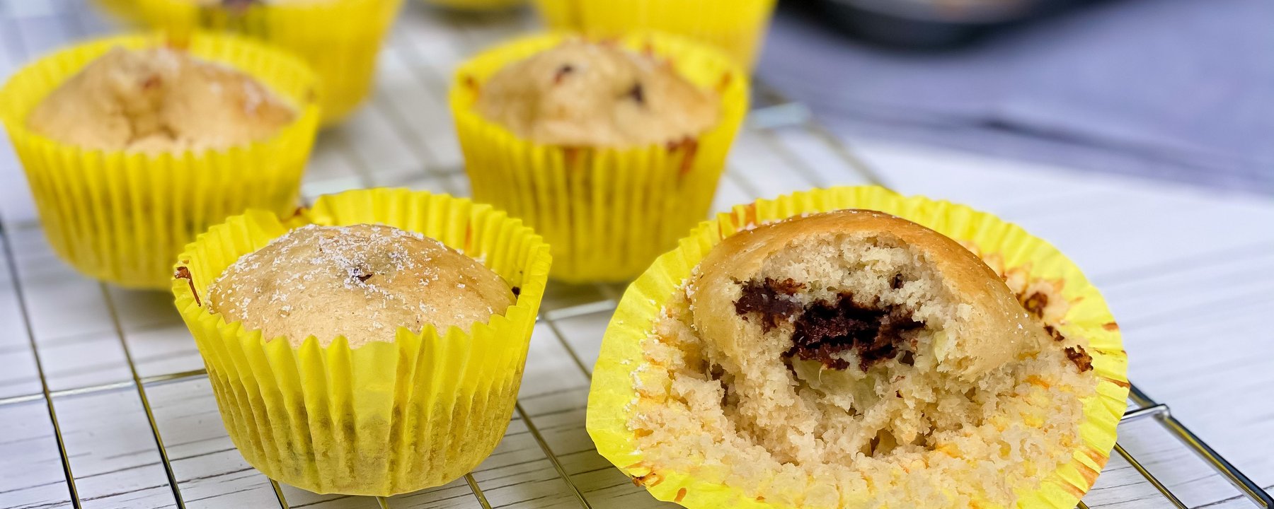 Mini muffins with dark chocolate filling in yellow cases on a cooling rack