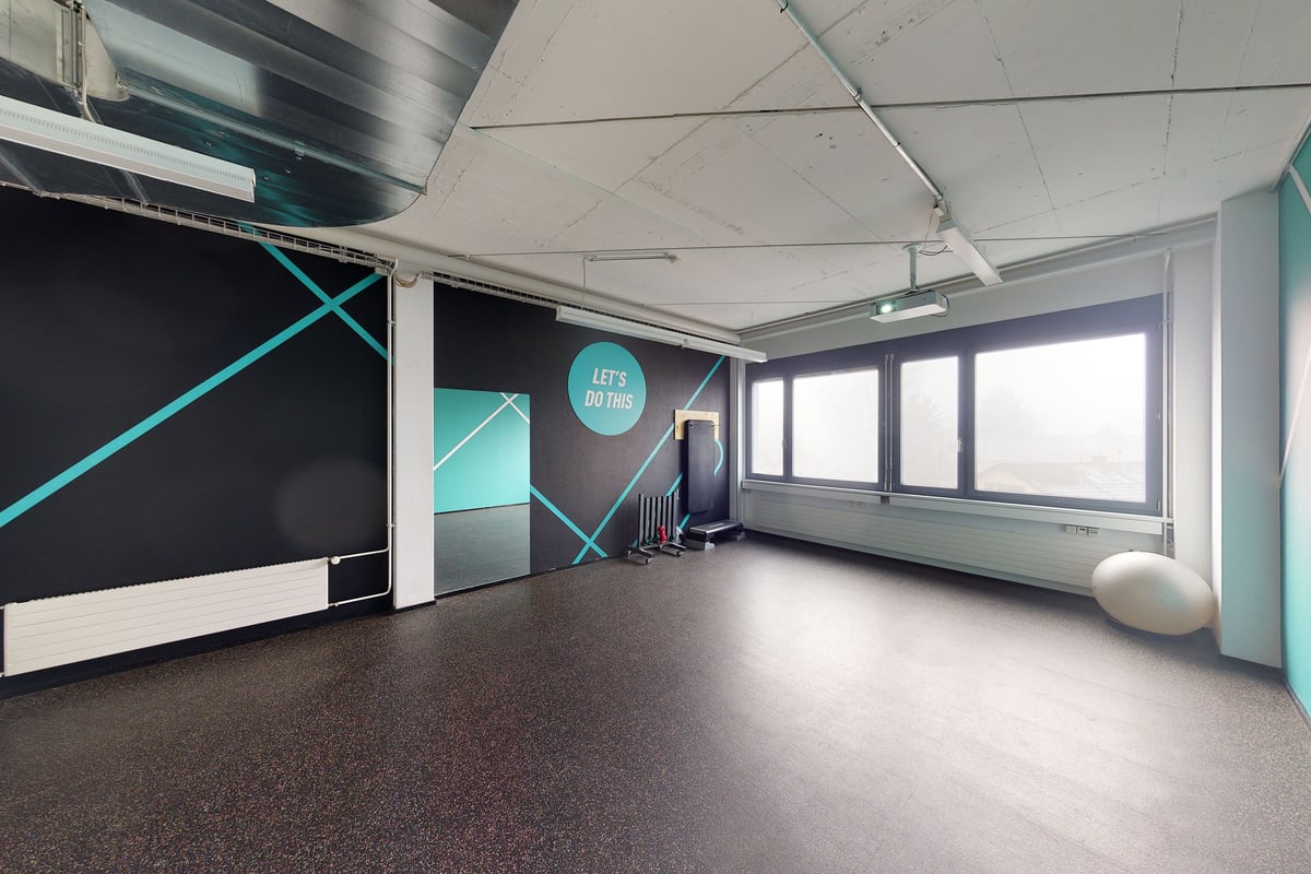 PureGym Uster: Studio de remise en forme avec des touches bleu sarcelle, des bancs rembourrés, des bandes de résistance et des fenêtres allant du sol au plafond.