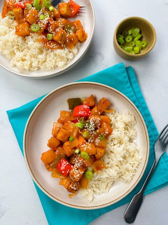 Two plates of sweet and sour tofu with rice, garnished with spring onions and sesame seeds