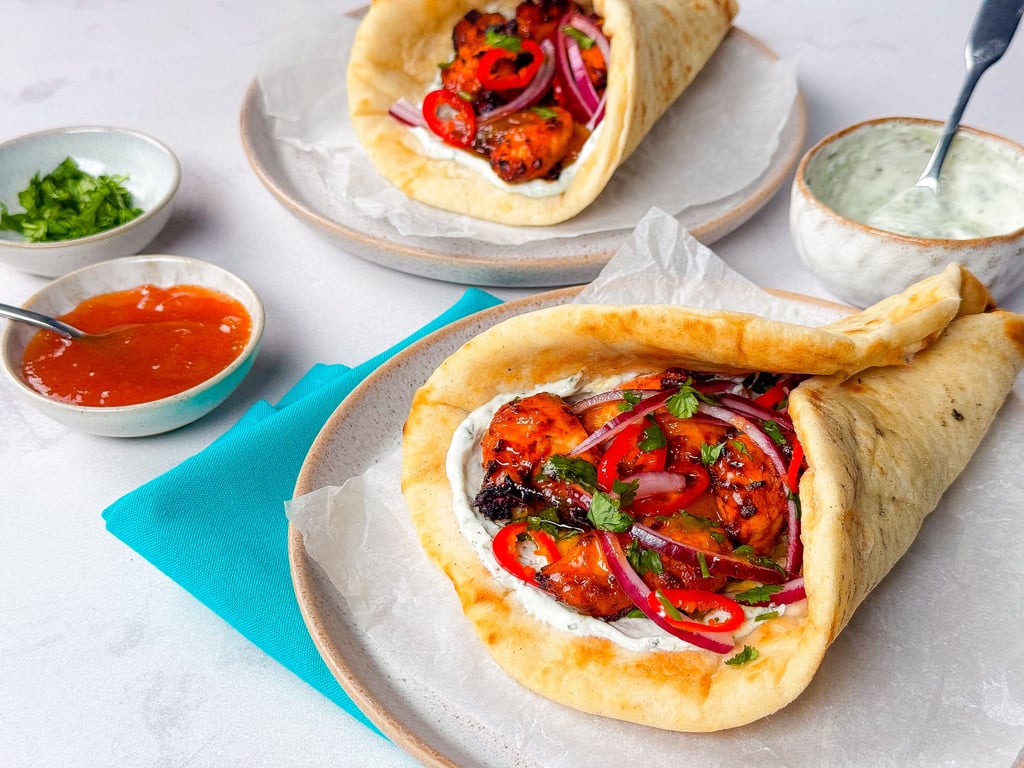 Two chicken wraps with red onions, chillies, and sauce on plates with dips nearby