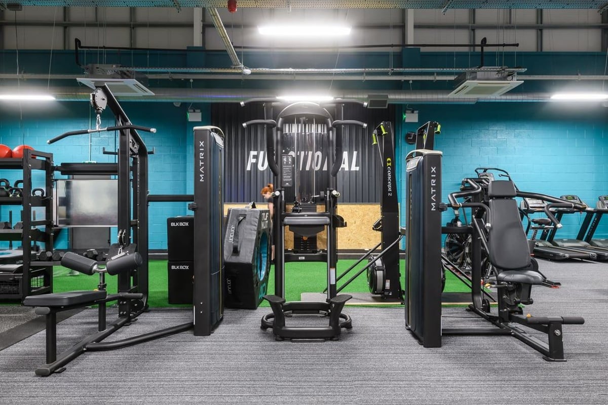 PureGym Buckingham: Strength machines, cable stations, benches, and rubberized flooring in a dimly lit gym.