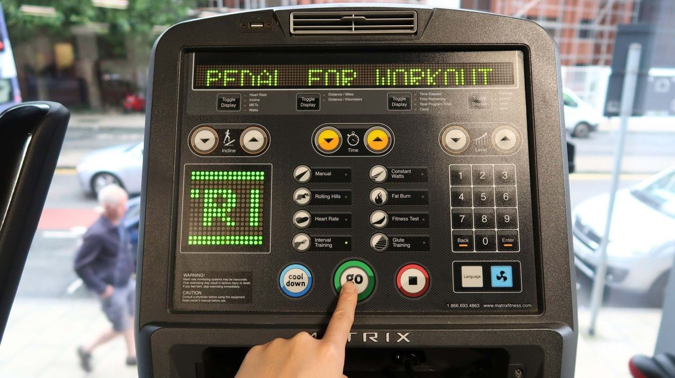 Finger pressing green go button on treadmill control panel with street view behind