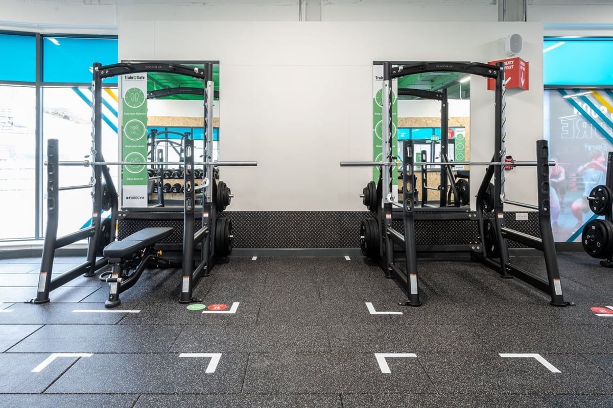 PureGym Aldershot Westgate Retail Park: Racks with resistance bands, squat racks, benches, and rubberized flooring in a gym.