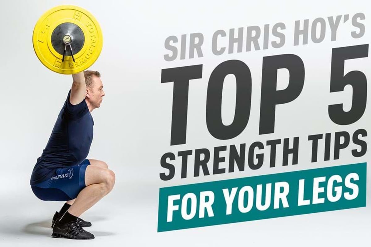 Man in navy sportswear squatting with a yellow barbell overhead against white background