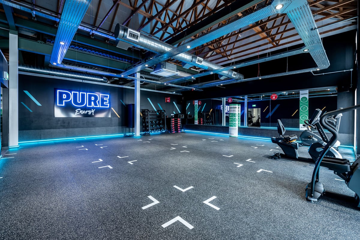 PureGym Chelmsford Meadows: Rows of treadmills, neon signage, steel beams with blue lighting, and floor markings.