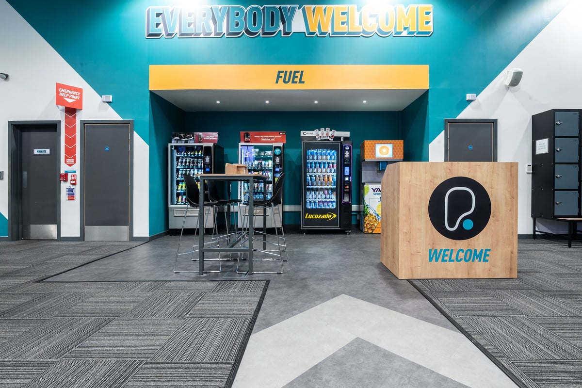 PureGym Dunfermline: Welcome area with tables and chairs, a fuel area with food and beverage vending, and a welcome podium.