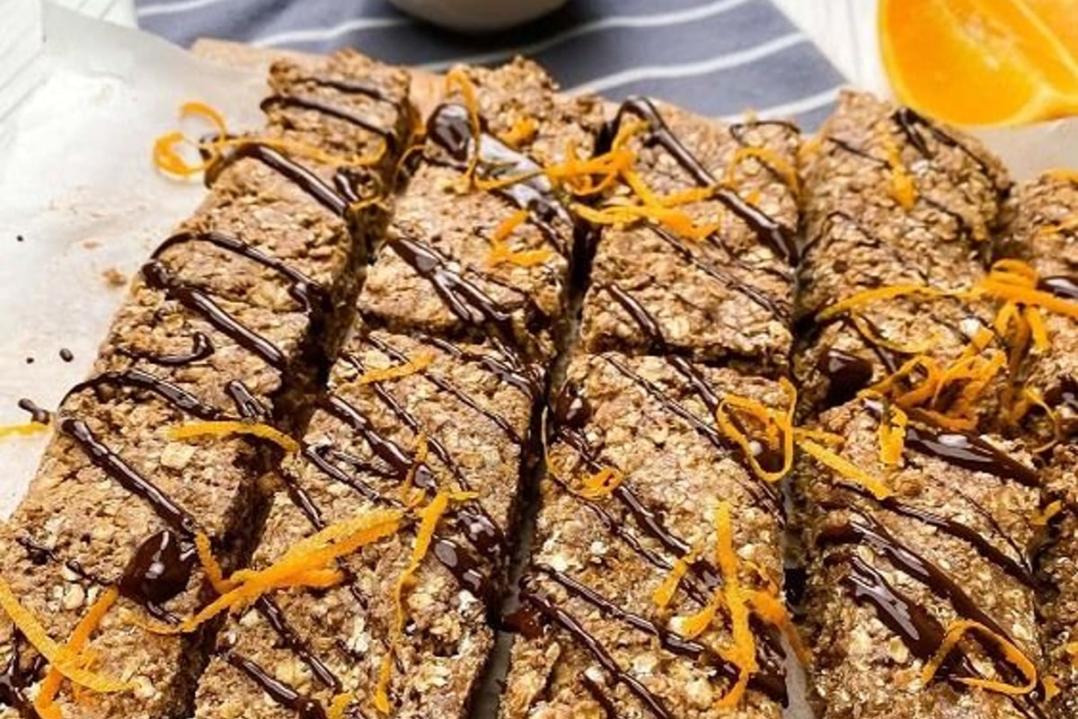 Oat bars drizzled with chocolate and orange zest on parchment with orange slices and sauce