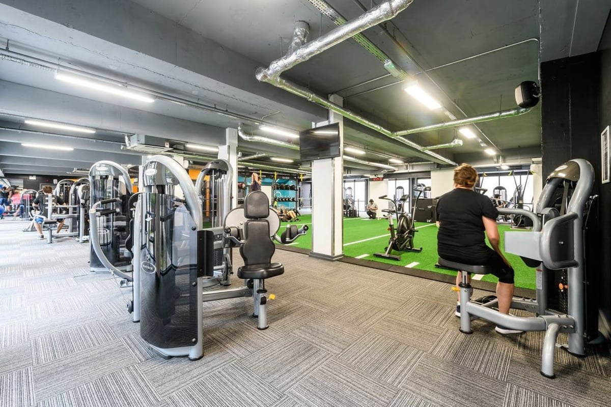 PureGym London Lambeth: Weight machines, free weights, turf area, and mirrored walls in a dimly lit gym interior.