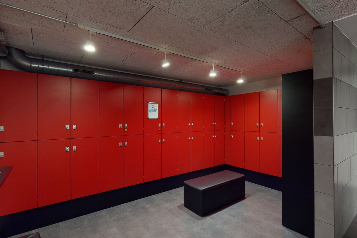 PureGym Aarau: Des casiers rouges, des luminaires et un banc dans les vestiaires d'un gymnase.