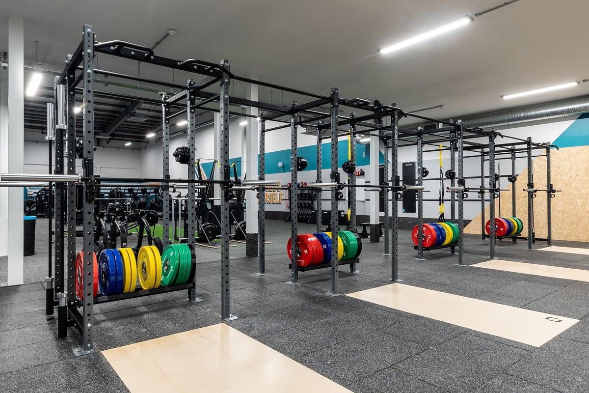 PureGym Watford Waterfields Retail Park: Racks with weights in varied colours, rubberized flooring, mirrors along walls.