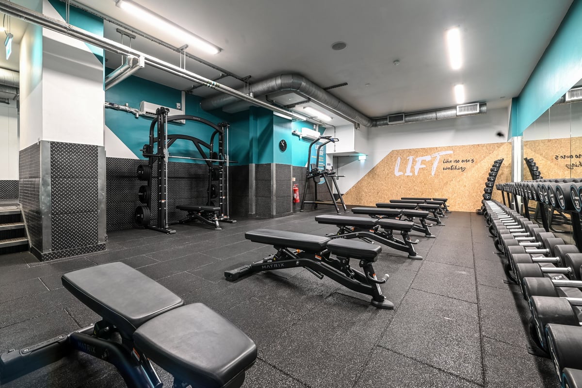 PureGym London Piccadilly: Weight racks, benches, mirrors, rubberised floor in teal-coloured gym studio.