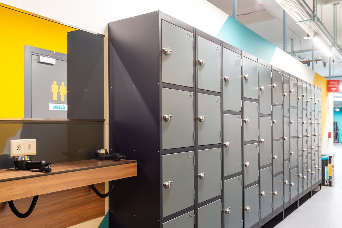 PureGym Wil: Des rangées de casiers gris et un miroir avec prises et sèche-cheveux.