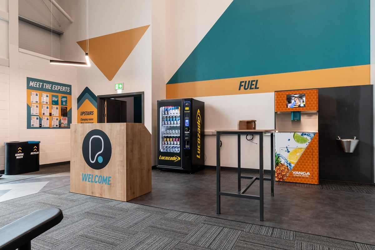 PureGym Caerphilly: Vending machines, seating area, with branding and product displays.