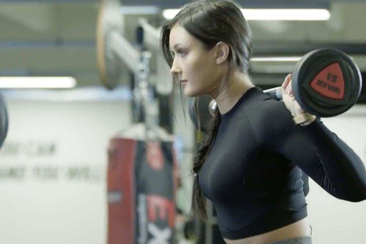 Woman lifting barbell weights on her shoulders in a gym setting