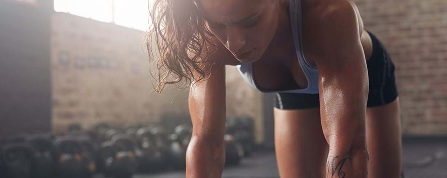 Woman in sportswear on hands and knees on a mat in a gym with kettlebells in background