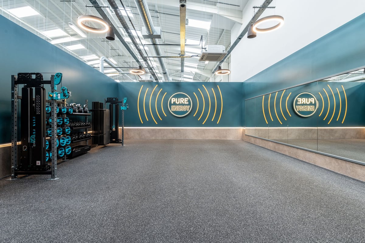 PureGym Keighley: Gym studio with weightlifting platforms, racks of dumbbells, mirrored walls, modern lighting fixtures.