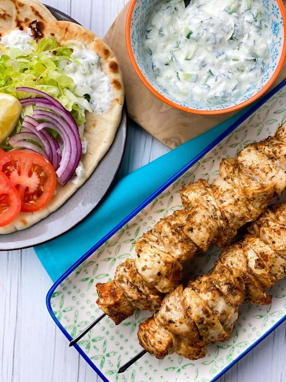 Grilled chicken skewers with flatbread topped with lettuce, tomato, onion, and tzatziki