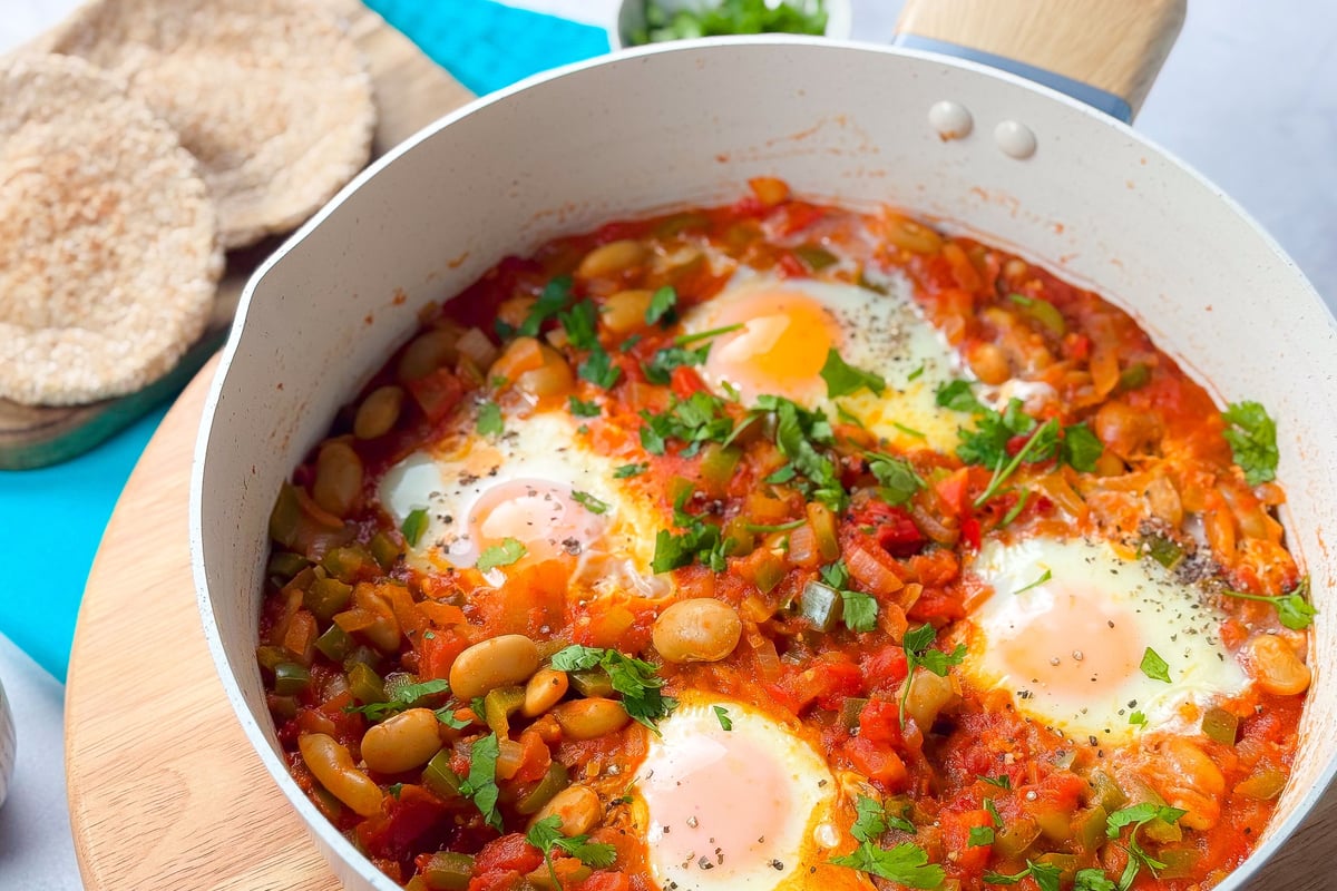 White pan with eggs poached in tomato sauce with butter beans and fresh herbs