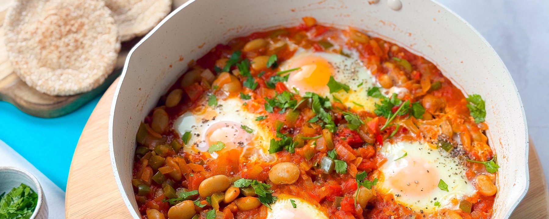 White pan with eggs poached in tomato sauce with butter beans and fresh herbs