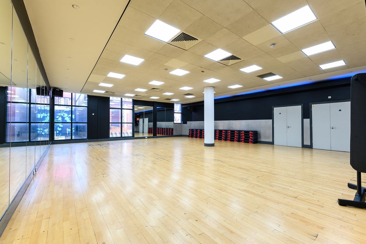 PureGym Norwich Riverside: Large empty studio space with wood flooring, floor-to-ceiling mirrors, and bench seating.