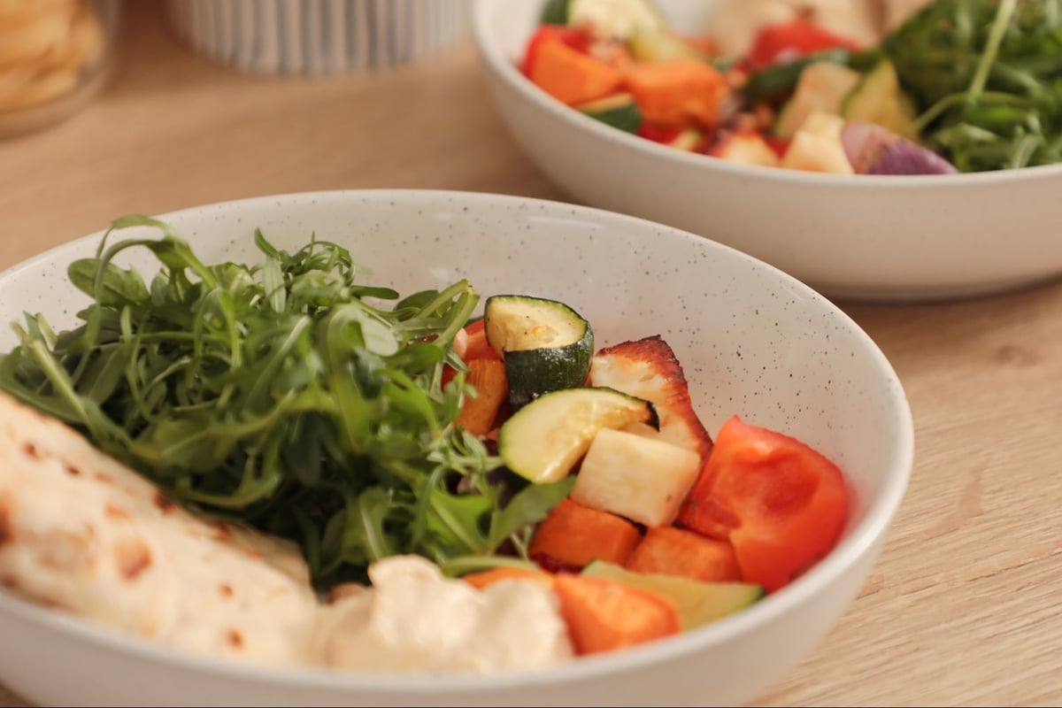 Bowl of grilled vegetables with rocket, halloumi and flatbread on wooden table