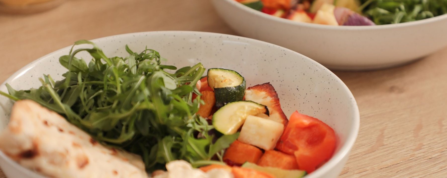Bowl of grilled vegetables with rocket, halloumi and flatbread on wooden table