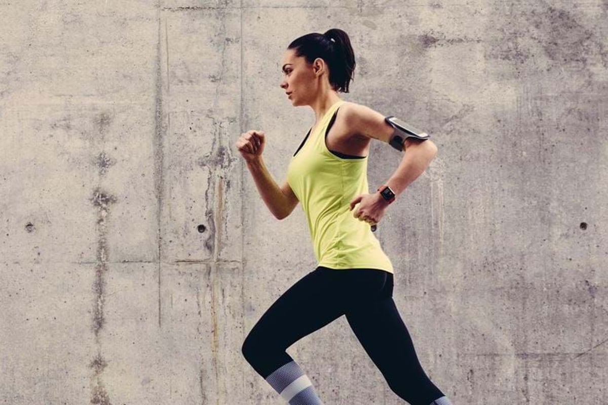 Woman in yellow top and black leggings running against a concrete wall background