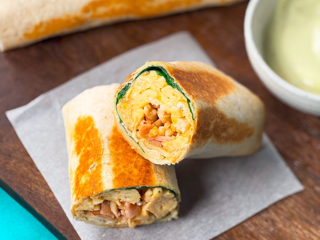Grilled breakfast wrap cut in half showing scrambled eggs, spinach, and bacon inside.