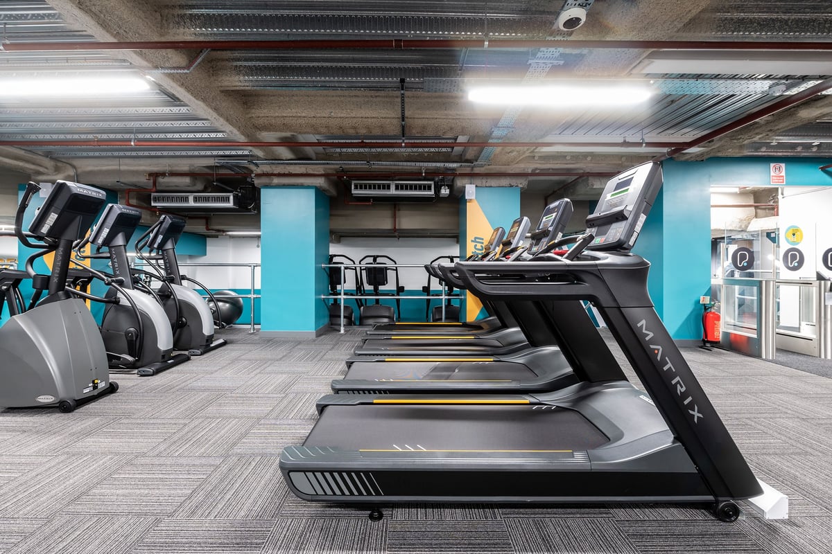 PureGym London Monument: Rows of treadmills, ellipticals, and exercise bikes in a gym with exposed ceiling pipes.